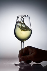 Hand holding glass of white wine with splash on gray