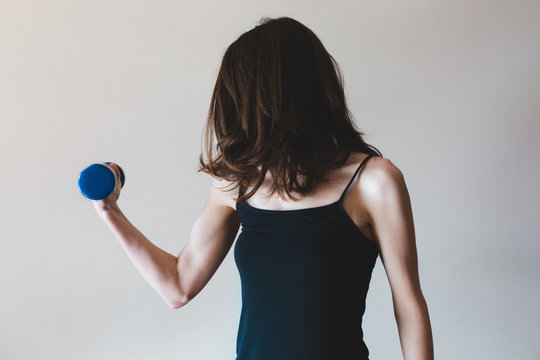 Thin woman flexing her muscle while holding a small dumbbell