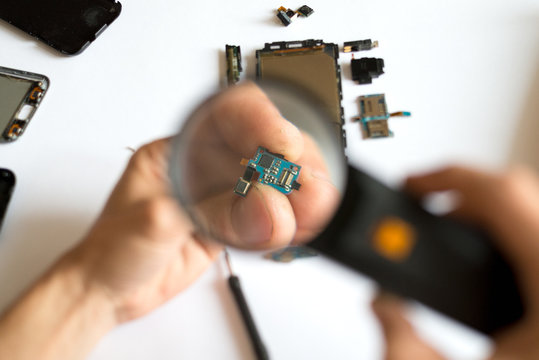Man using magnifying glass on cellphone chip
