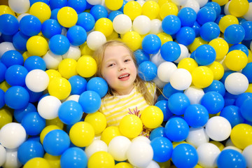 Obraz na płótnie Canvas Happy little girl having fun in ball pit in kids indoor play center. Child playing with colorful balls in playground ball pool.