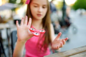 Cute school girl playing with colorful fidget spinner - obrazy, fototapety, plakaty