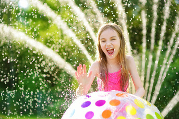 Adorable little girl playing with a sprinkler in a backyard on sunny summer day. Cute child having fun with water outdoors.