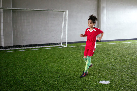 Young kid having fun playing indoor football on turf