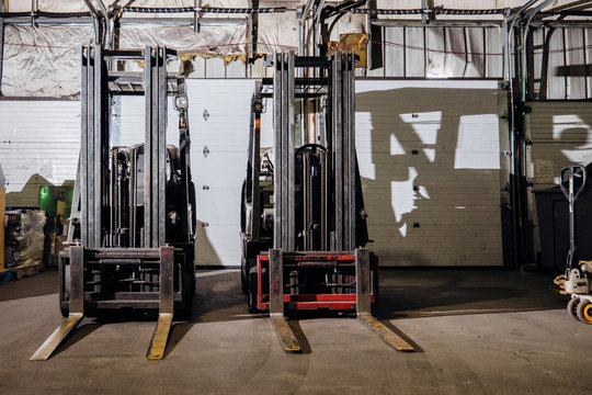 Two forklifts sitting side by side in a warehouse.