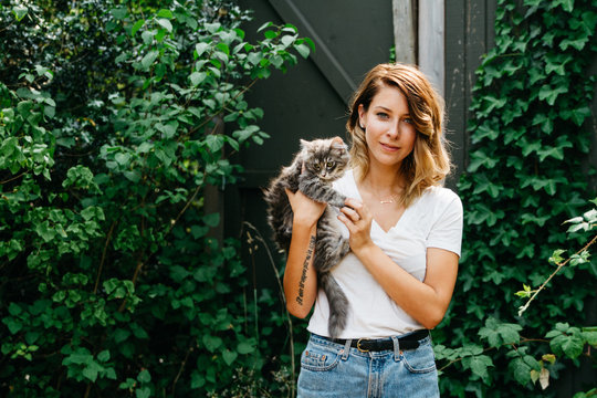 young woman holding cute cat outdoors in front of ivy wall