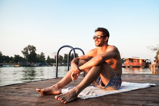 Caucasian man sunbathing on wooden dock with horizon in background.