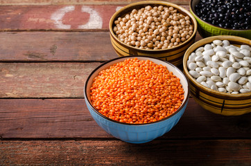 Assorted beans in bowls with red lentil, chick-pea and kidney bean on wooden background.