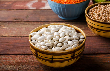 Assorted beans in bowls with red lentil, chick-pea and kidney bean on wooden background.