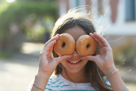 Young girl with two doughnuts covering her face and looking at camera