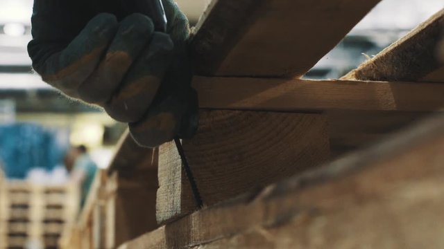 Carpeter man hand puts screw into wooden pallet structure using screwdriver in workshop, close up