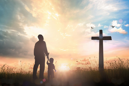 Resurrection of Easter Sunday concept: Silhouette father and son looking for the cross on meadow sunrise background.