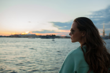 Young and beautiful girl sitting on the embankment of the river. she looks at the sunset and ships...