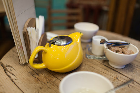 Yellow kettle with tea on the table in a café next to a dish full of brown sugar