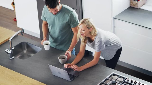 Overhead View Of Couple Looking At Laptop In Modern Kitchen