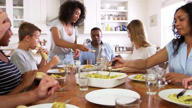 Two Families With Teenage Children Eating Meal In Kitchen
