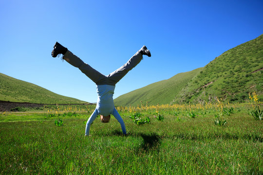 Woman Doing A Handstand On Mountain Meadow