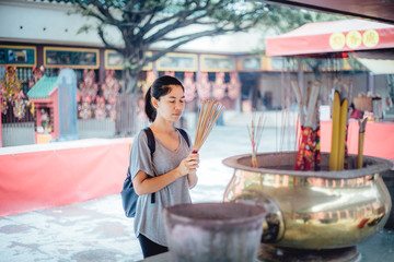 Asian girl praying outdoor at a temple, offering incense sticks