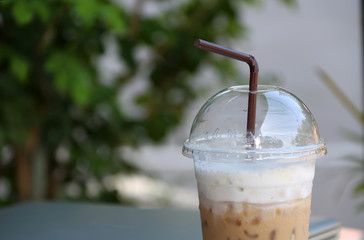 Close up ice coffee in the plastic cup with brown straw and out focus notebook, start work in a...