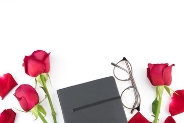 Red roses, glasses and black notebook on white background with copy space