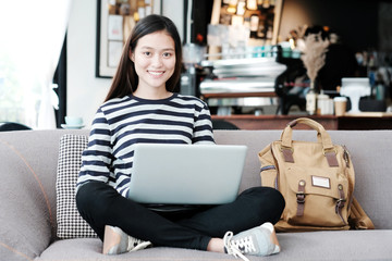 Beautiful asian girl using laptop computer while sitting on sofa with smiling face emotion, people and technology concept, lifestyle