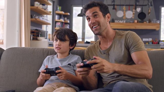 Father And Son Sitting On Sofa In Lounge Playing Video Game