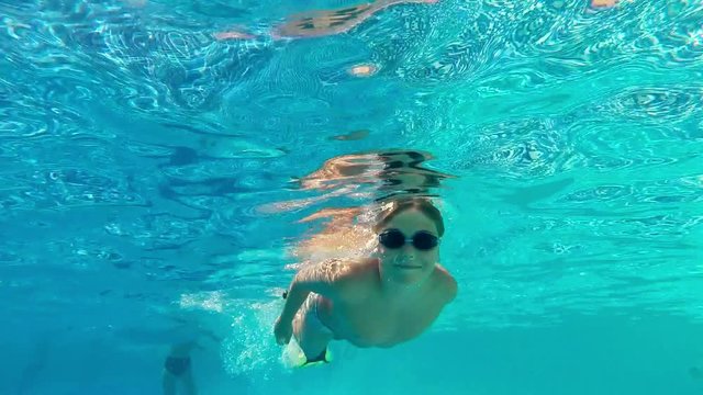 Caucasian swimmer child teen boy floats, dives in sunny pool with clear water at tourist resort. Active rest and healthy lifestyle, water sports in vacation holiday. Underwater survey, slow motion