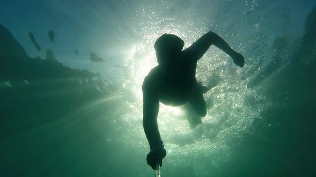 Caucasian swimmer male dives iinto the sea depths under water in glare of sunlight at tourist resort. Active rest and healthy lifestyle, water sports in holiday. Underwater slow motion
