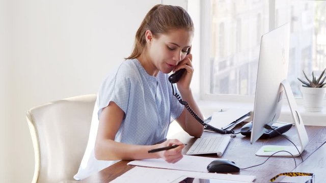 Young white woman on the phone, smiling at her office desk