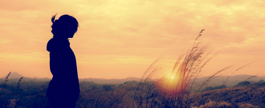 A woman standing alone in sunset scene.