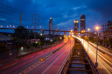 Traffic on city road through modern buildings at twilight in Thailand. Long exposure shot photography by DSLR camera.