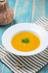 Pumpkin and carrot soup with cream and parsley on blue  wooden background.
