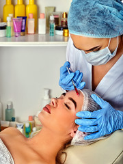 Obraz na płótnie Canvas Filler injection for woman forehead face. Plastic aesthetic facial surgery by doctor in beauty clinic. Doctor in medical gloves with syringe. Skin tightening. Cosmetics in bottles in the background.