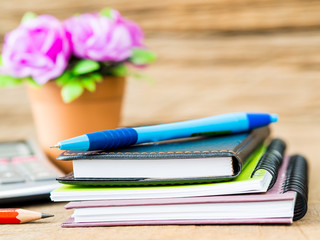Office accessories including note books, blue pen, calculator and flower  on wooden background. Education and business concept.