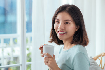 Young pretty woman sitting at opened window drinking coffee