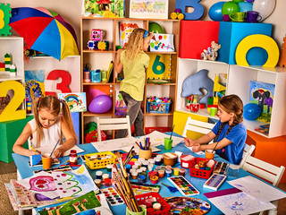 Kids playroom organization of children painting and drawing in kid's club. Craft lesson in primary school. Kindergarten teacher and students work together. Preparation for an art exhibition.
