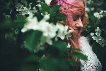 The beautiful girl with pink hair walks among the blossoming apple-tree in the summer