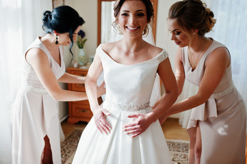 Bridesmaids helping gorgeous bride to dress up and get ready for her wedding ceremony.
