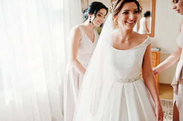 Naklejka premium Bridesmaids helping gorgeous bride to dress up and get ready for her wedding ceremony.