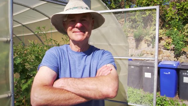 Portrait Of Senior Male Gardener Outside Allotment Greenhouse