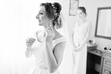 Fabulous young bride posing with her bridesmiads in her room on the wedding day. Black and white photo.