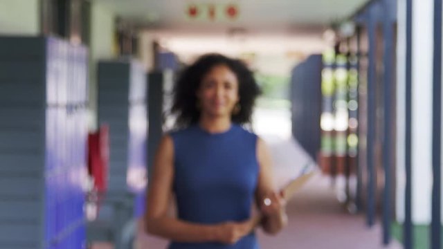 Black female teacher walks into focus in school corridor