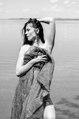 Gorgeous young brunette woman in blue fabrics, poses on the shore of the water, relaxes and shows herself in all its glory demonstrating a beautiful and well-proportioned figure