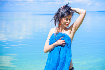 Gorgeous young brunette woman in blue fabrics, poses on the shore of the water, relaxes and shows herself in all its glory demonstrating a beautiful and well-proportioned figure