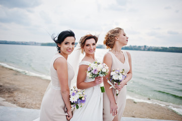 Stunning bride with pretty bridesmaids posing with bouquets on the lakeside.