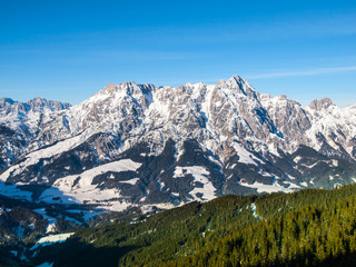 High rocky snowy peak on sunny winter day with blue sky. Alpine mountain ridge.