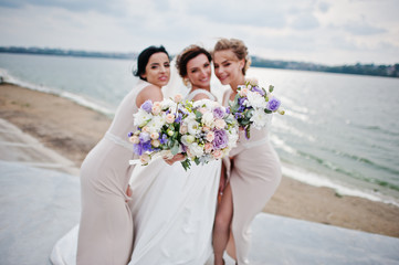 Stunning bride with pretty bridesmaids posing with bouquets on the lakeside.