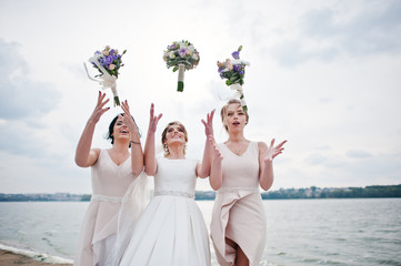 Stunning bride with pretty bridesmaids posing with bouquets on the lakeside.