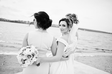 Stunning bride with pretty bridesmaids posing with bouquets on the lakeside. Black and white photo.