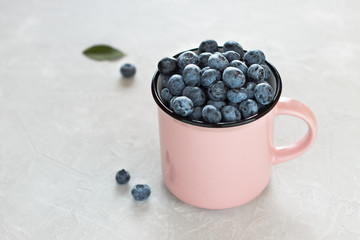 Fresh blueberries in pink mug or cup on light gray background.