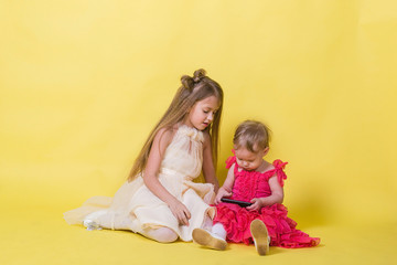 Fototapeta na wymiar Two sisters in dresses on a yellow background and a mobile smartphone